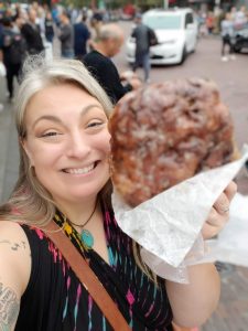 Cat is holding an apple fritter in the street outside of Pike's Public Market in Seattle, Washington.